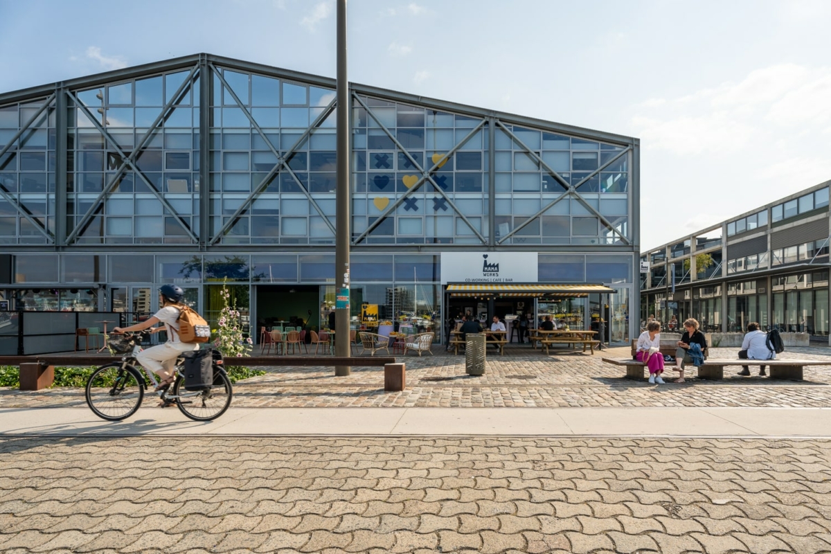 Vue de la facade vitrée du Mama Works depuis la zone piétonne extérieur. Le bâtiment est ouvert sur une terrasse. On aperçoit une piste cyclable en premier plan.
